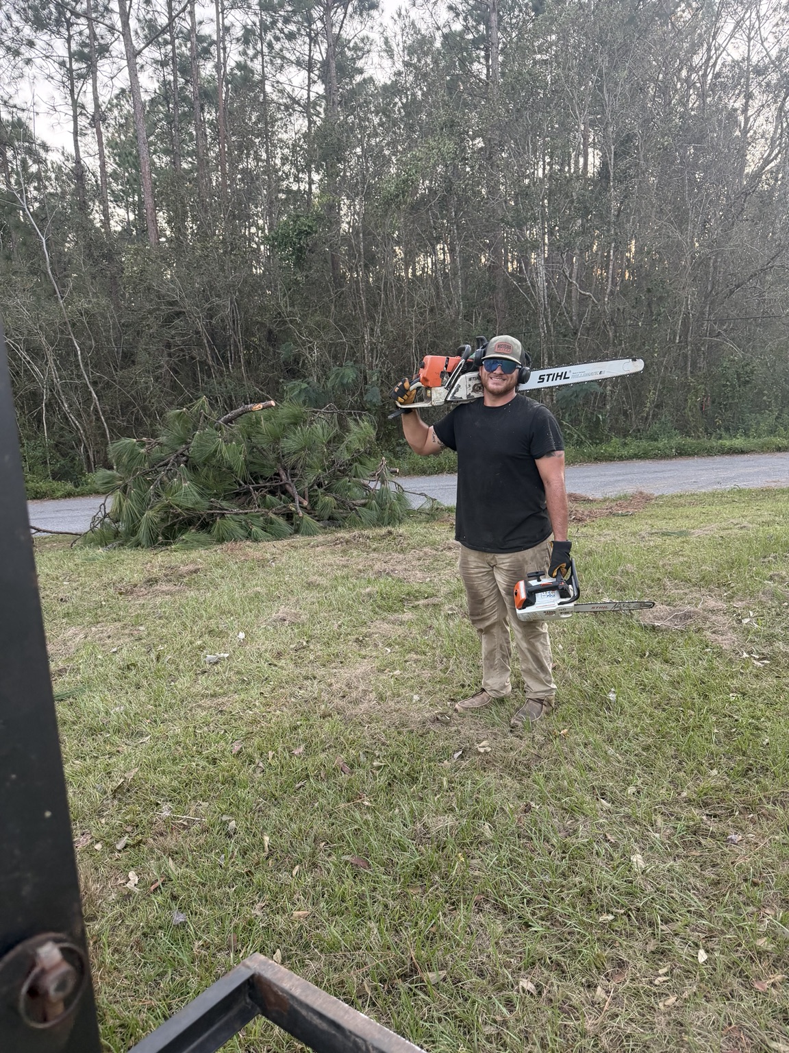 Team member with tree service equipment beside a pile of cut branches